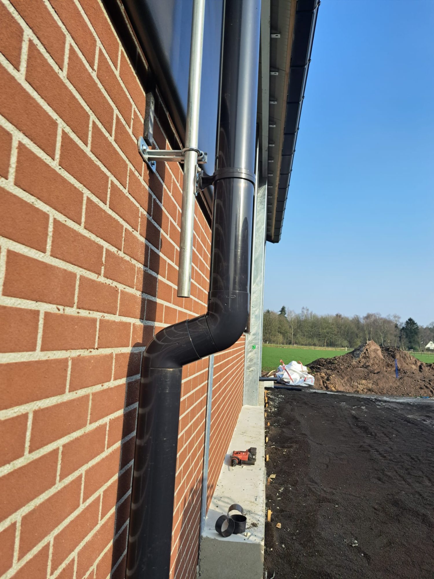 Detail van een aluminium hemelwaterafvoer langs een bakstenen gevel