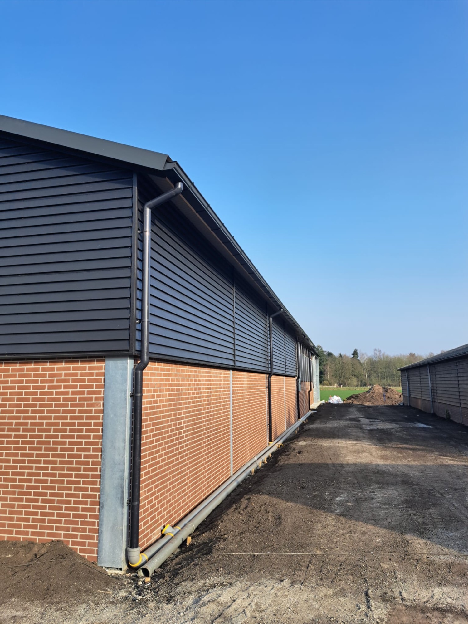 Aluminium dakgoot op een loods met zwarte houten gevel en metselwerk